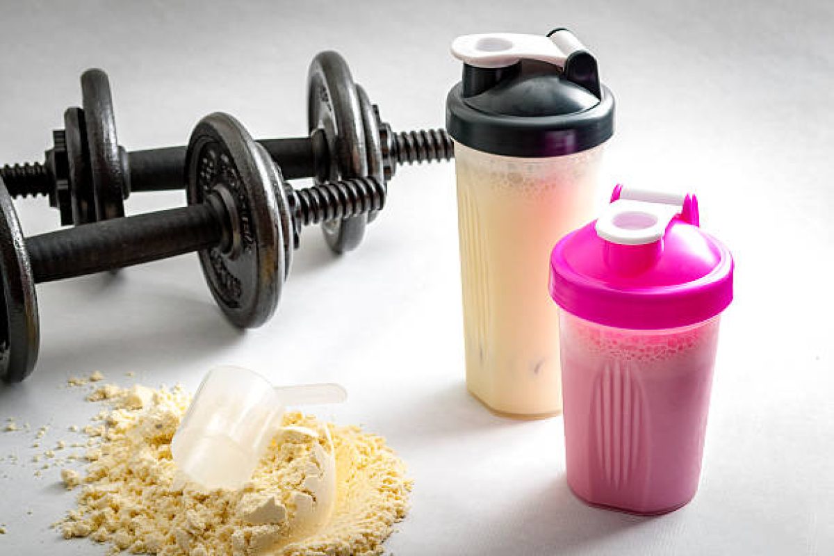 Fitness and workout concept with dumbbells, protein shakers  and a scoop in protein powder. The two shakers have black and pink lids and the background is white